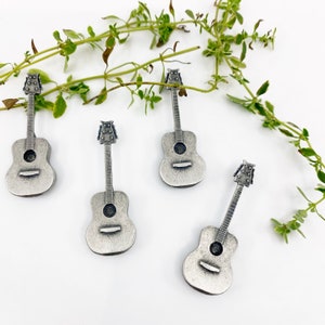 May include: Five silver-colored miniature acoustic guitars on a white background. The guitars are arranged in a semi-circle with the tips of the guitars pointing towards the center of the circle.