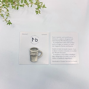 May include: A silver pewter mug with a leaf design on the side. The mug is a miniature sculpture designed and reworked by Michelle Beaudoin. The mug is a magnet and can be used on fridges, lockers, or magnetic frames and boards. Handmade in Canada.