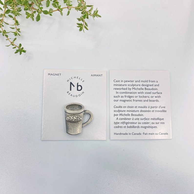 May include: A silver pewter mug with a leaf design on the side. The mug is a miniature sculpture designed and reworked by Michelle Beaudoin. The mug is a magnet and can be used on fridges, lockers, or magnetic frames and boards. Handmade in Canada.