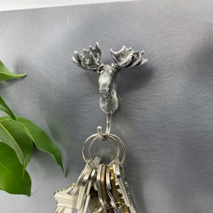 May include: Silver moose head wall hook with a set of keys hanging from it.