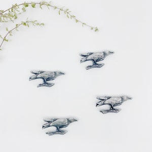 Peut inclure: Quatre figurines de corbeaux en argent avec des ailes détaillées et perchées sur une branche. Les corbeaux sont disposés de manière symétrique sur un fond blanc.
