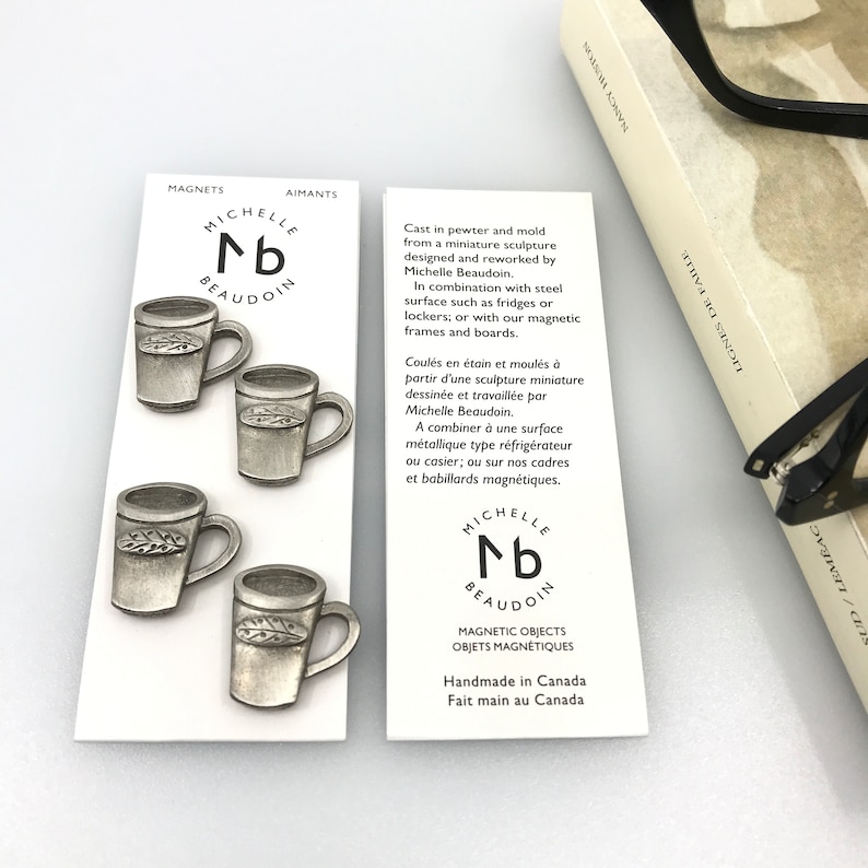 May include: Four silver-toned metal mugs with a leaf design. The mugs are magnetic and are packaged with a white card that reads "Michelle nb Beaudoin" and "Magnetic Objects, Handmade in Canada".