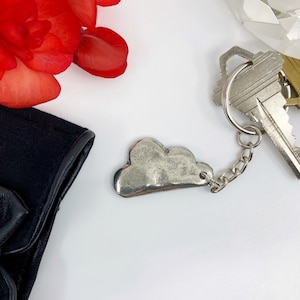 May include: A silver cloud-shaped keychain with a silver chain attached to a silver key.