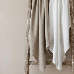 Pu&ograve; includere: Una scala in legno rustico a due pioli sostiene due coperte piegate. Una coperta &egrave; di colore beige chiaro a tinta unita, l'altra &egrave; di colore bianco a tinta unita. Entrambe le coperte presentano un tessuto morbido e testurizzato che cade verticalmente.