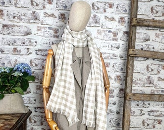 Könnte beinhalten: Ein beiges Leinenkleid mit einem weißen und beigen Gingham-Schal. Das Kleid hat eine lockere Passform und eine lange Länge. Der Schal ist um den Hals gebunden und hängt an der Vorderseite des Kleides herunter.