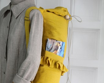 Puede incluir: Una bolsa de yoga de lino amarilla con cierre de cordón y un detalle de volantes. La bolsa tiene un bolsillo en la parte delantera y una cuenta de madera en el cordón.