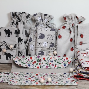 May include: A collection of small linen bags with various animal and floral prints. The bags are tied with twine and wooden beads. The bags are arranged on a wooden surface.