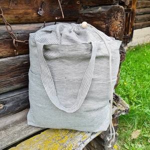 Peut inclure: Un sac cabas en lin rayé avec une fermeture à bouton en bois. Le sac est posé sur un banc en bois usé.