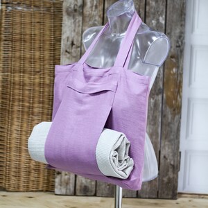 May include: A lavender linen tote bag with a rolled towel inside. The bag has a pocket on the front and is hanging from a clear plastic mannequin.