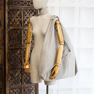 May include: A beige linen tote bag with a wooden mannequin wearing a beige linen shirt. The bag is draped over the mannequin's shoulder and arm.