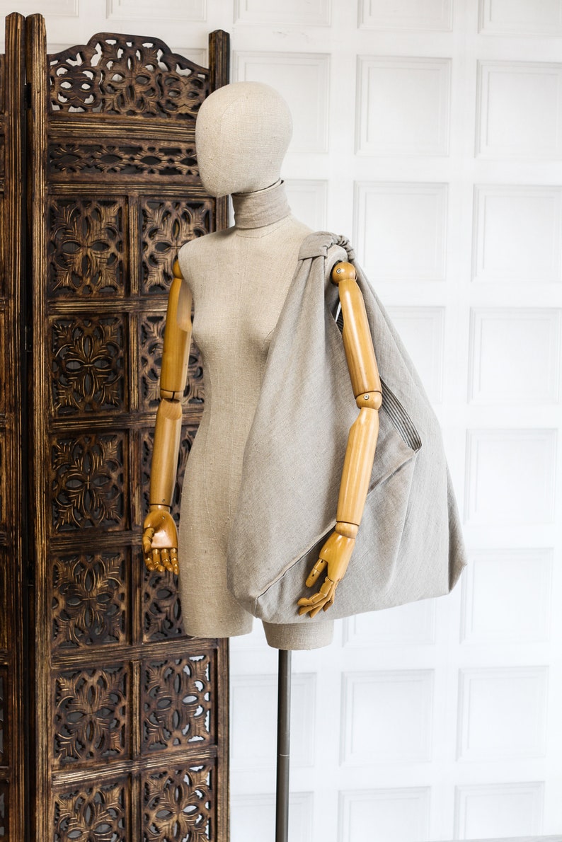 May include: A beige linen tote bag with a wooden mannequin wearing a beige linen shirt. The bag is draped over the mannequin's shoulder and arm.