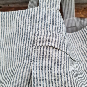 May include: A striped tote bag made of a natural fabric with blue stripes. The bag has two straps and a pocket on the front.