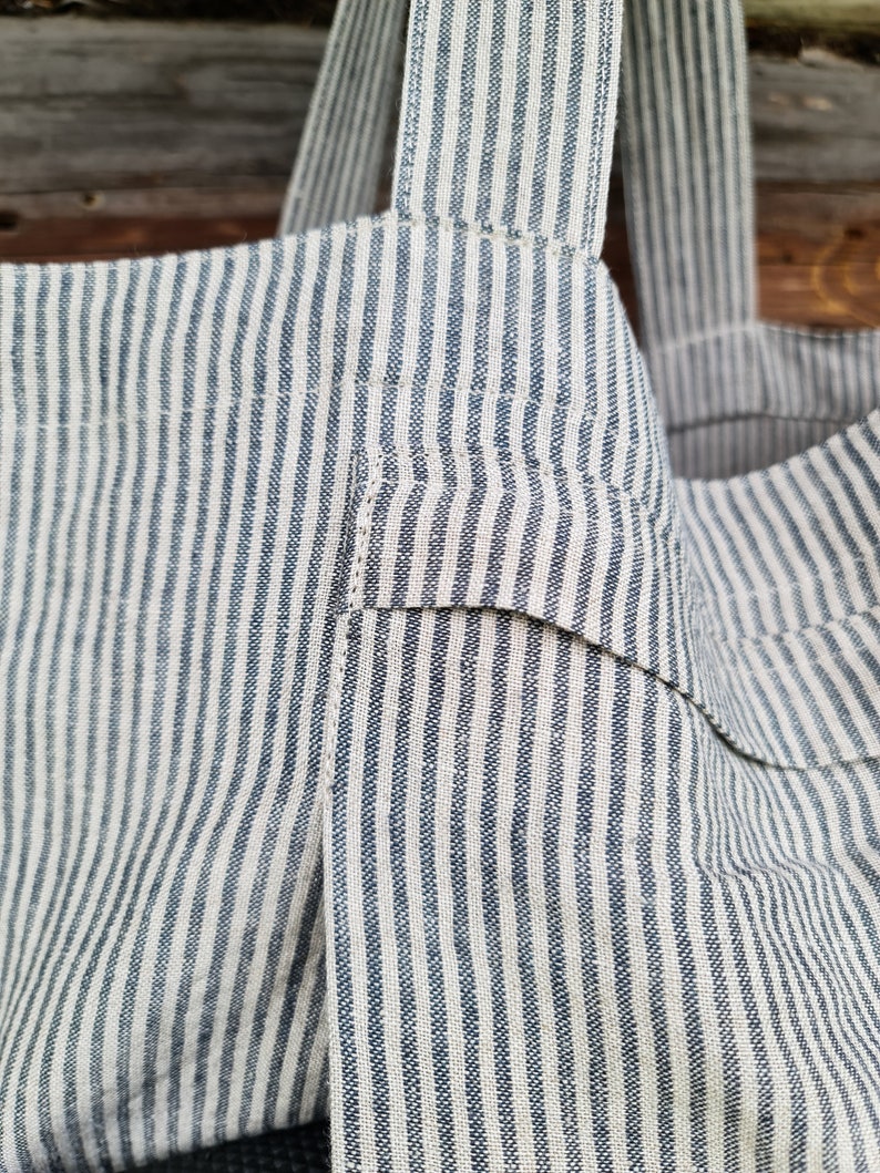 May include: A striped tote bag made of a natural fabric with blue stripes. The bag has two straps and a pocket on the front.