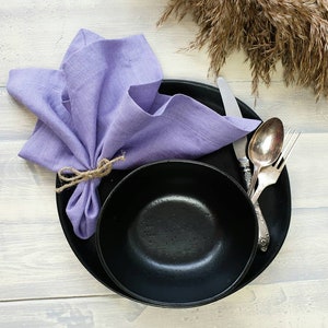 May include: A black bowl and plate with a purple linen napkin tied with twine. The word "Violet" is written in white on a light wood background.