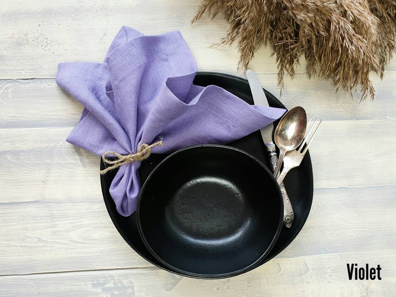 May include: A black bowl and plate with a purple linen napkin tied with twine. The word "Violet" is written in white on a light wood background.