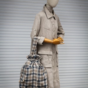 May include: A beige linen coat with a checkered tote bag. The bag has a drawstring closure and wooden bead accents.