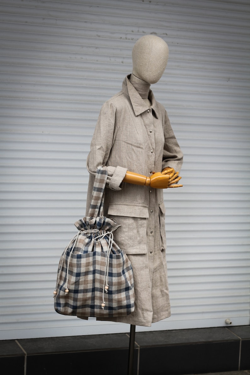 May include: A beige linen coat with a checkered tote bag. The bag has a drawstring closure and wooden bead accents.