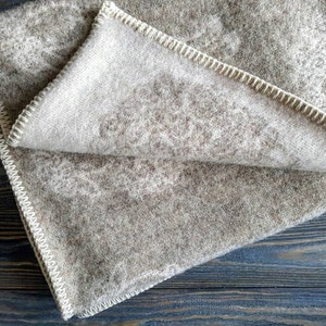 May include: A brown and white wool blanket with a white stitched border. The blanket is folded in half and has a soft, fuzzy texture.