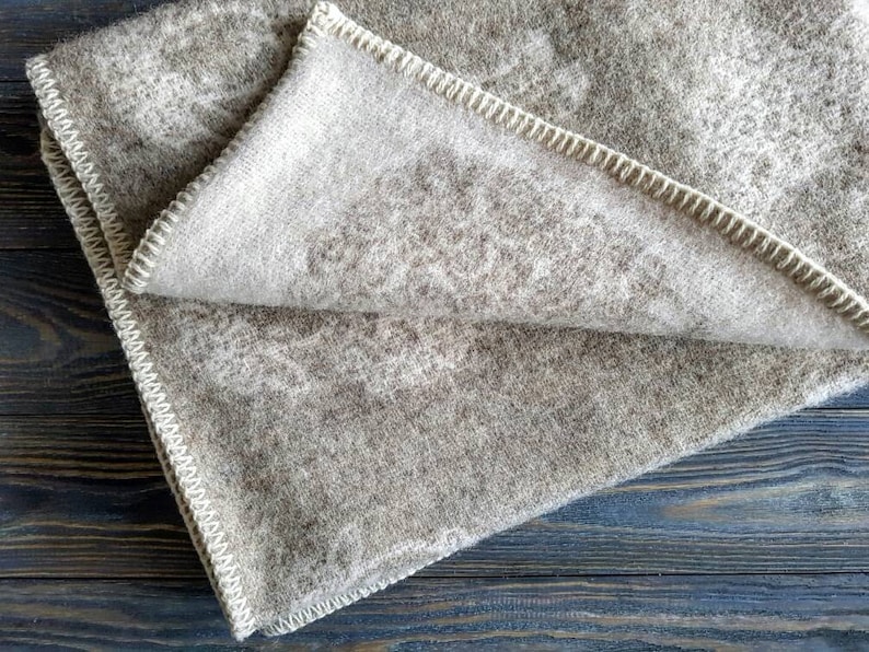 May include: A brown and white wool blanket with a white stitched border. The blanket is folded in half and has a soft, fuzzy texture.