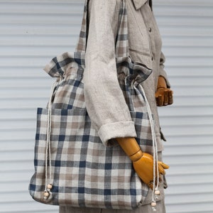May include: A large, brown and blue plaid tote bag with a drawstring closure and wooden bead accents on the straps.