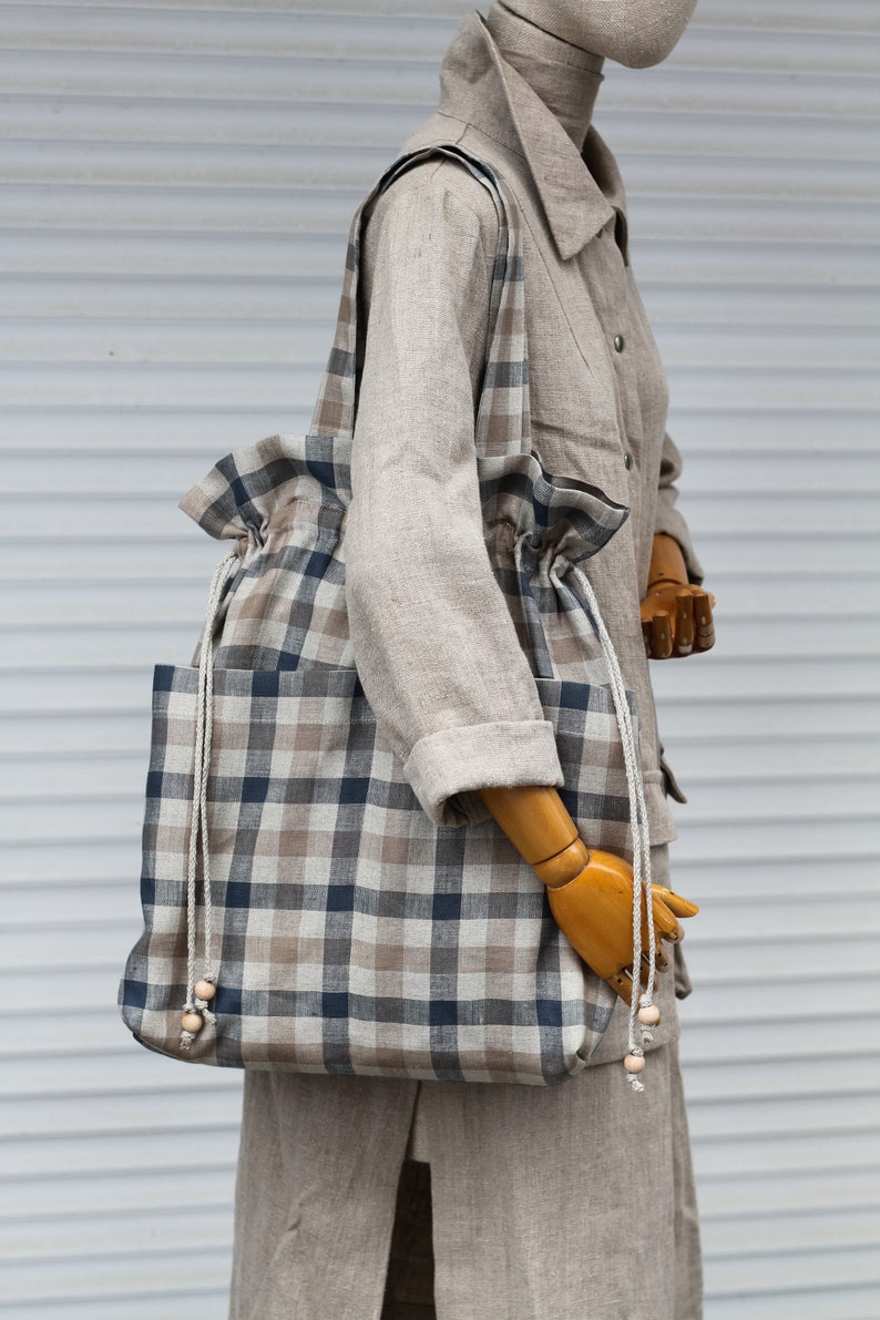May include: A large, brown and blue plaid tote bag with a drawstring closure and wooden bead accents on the straps.