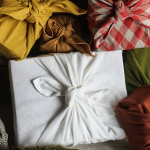 May include: A collection of gifts wrapped in various fabrics, including a white fabric, a yellow fabric, a brown fabric, a red and white checkered fabric, a green fabric, and a brown fabric. The gifts are tied with knots and bows.