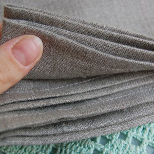 Pu&ograve; includere: Una pila di tovaglioli in tessuto marrone chiaro piegati con una trama visibile. Ogni tovagliolo presenta bordi dritti cuciti lungo l'orlo, che mettono in risalto la trama naturale del materiale tessile in una tonalit&agrave; neutra e terrosa.