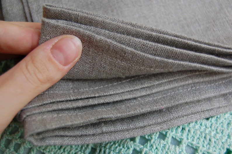 Pu&ograve; includere: Una pila di tovaglioli in tessuto marrone chiaro piegati con una trama visibile. Ogni tovagliolo presenta bordi dritti cuciti lungo l'orlo, che mettono in risalto la trama naturale del materiale tessile in una tonalit&agrave; neutra e terrosa.