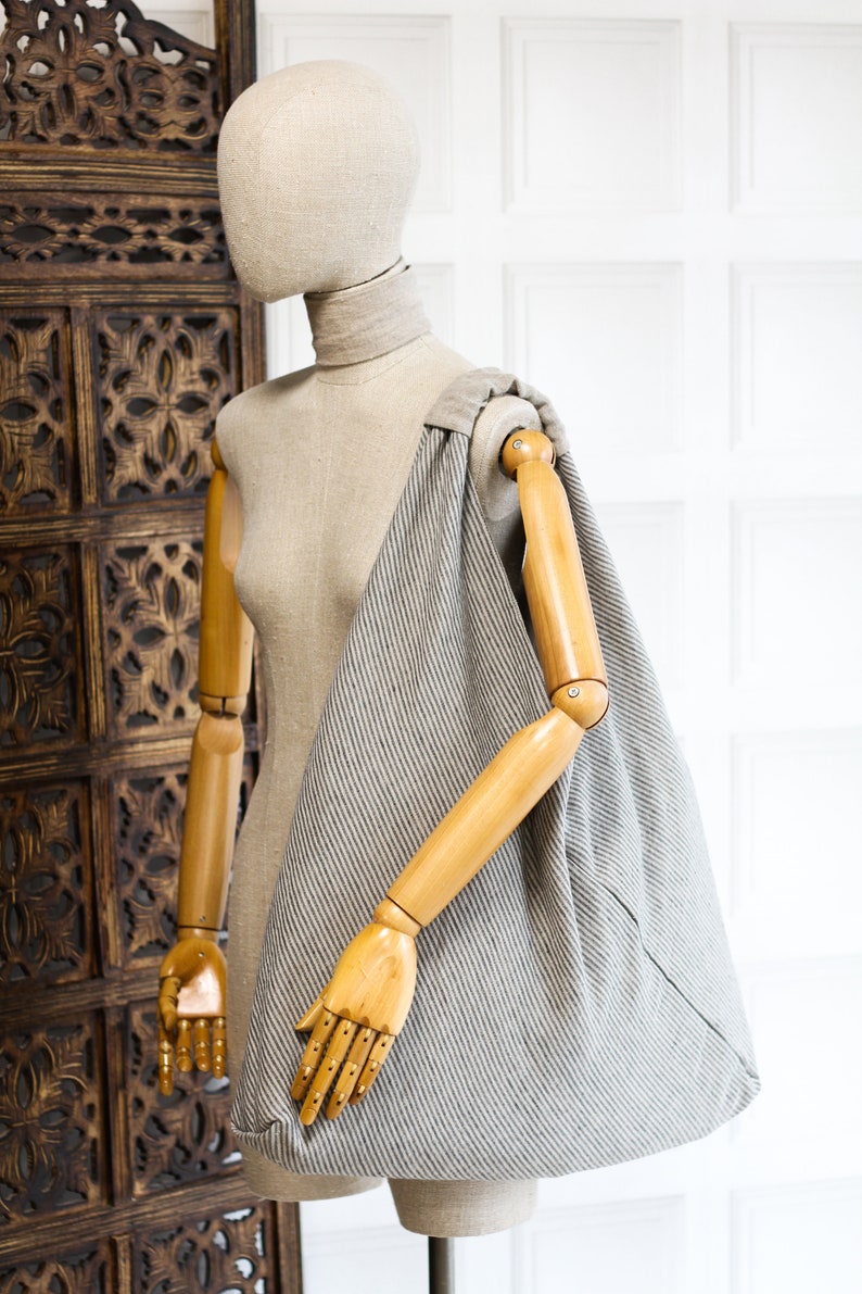 May include: A gray and white striped tote bag with a wooden handle. The bag is hanging on a wooden mannequin.