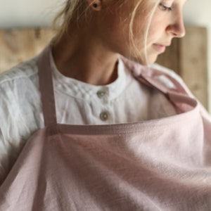 Pu&ograve; includere: Un copriallattamento in lino rosa chiaro con un cinturino in lino bianco. Il copriallattamento &egrave; drappeggiato sulle spalle di una persona.
