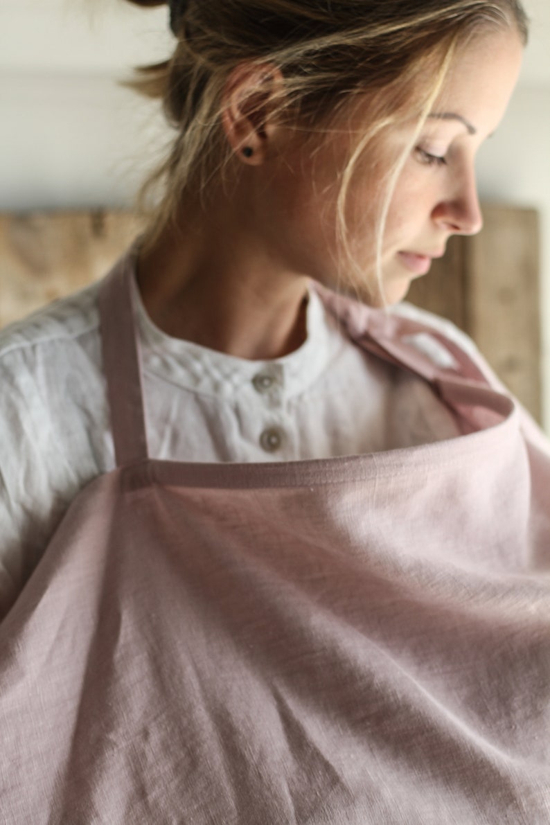 Pu&ograve; includere: Un copriallattamento in lino rosa chiaro con un cinturino in lino bianco. Il copriallattamento &egrave; drappeggiato sulle spalle di una persona.