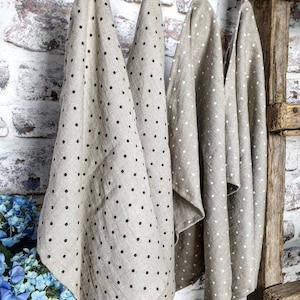 May include: Four linen tea towels hanging on a rustic wooden ladder. The towels are beige with black polka dots.