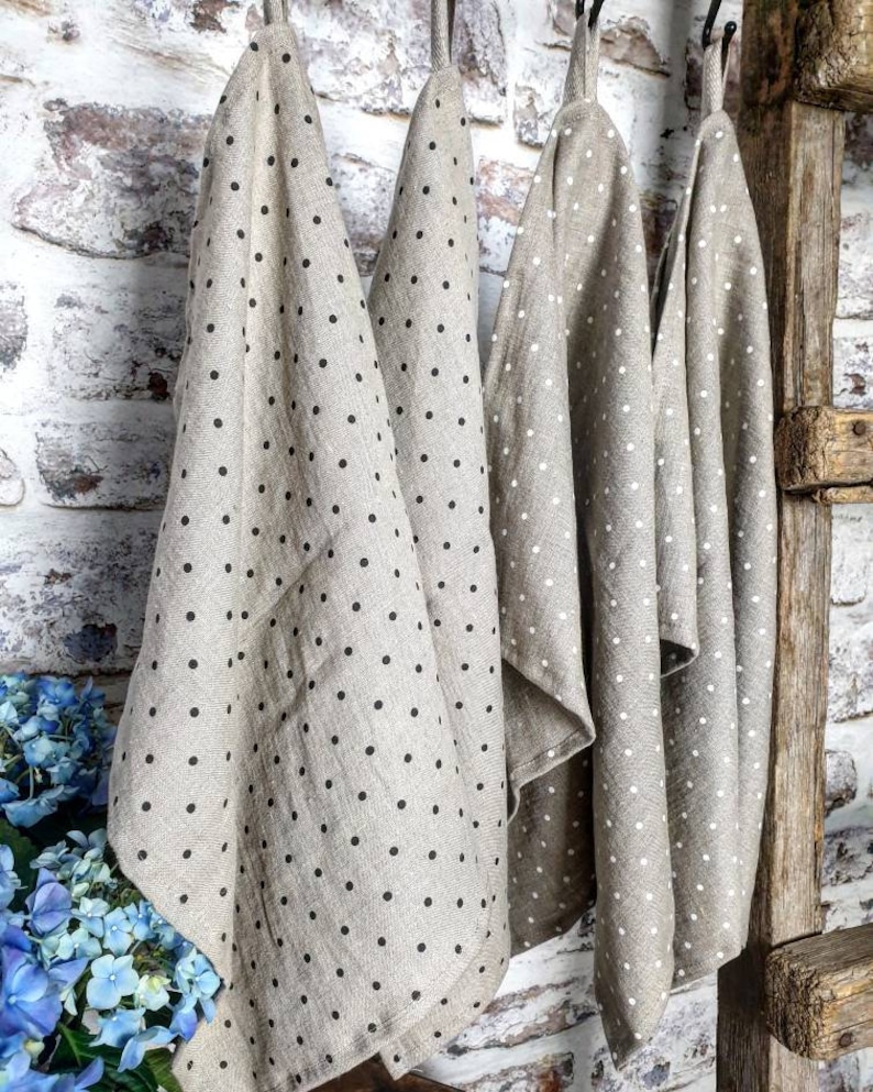 May include: Four linen tea towels hanging on a rustic wooden ladder. The towels are beige with black polka dots.