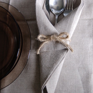 May include: A linen napkin folded into a triangle shape with a fork, knife, and spoon inside. The napkin is tied with twine at the center.