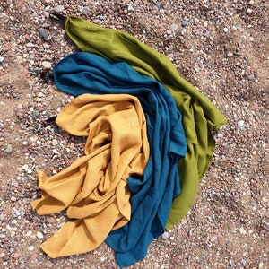 May include: Three fabric squares in different colors: mustard yellow, teal blue, and olive green. The squares are folded and layered on top of each other, creating a colorful and textured display.