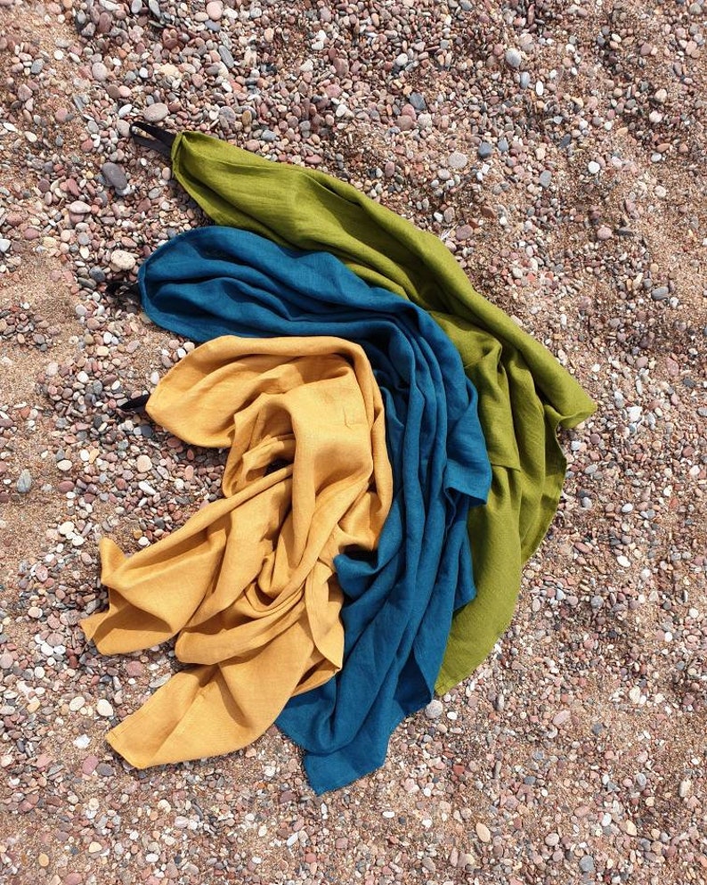 May include: Three fabric squares in different colors: mustard yellow, teal blue, and olive green. The squares are folded and layered on top of each other, creating a colorful and textured display.
