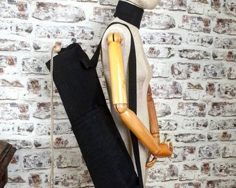May include: A black yoga mat carrier with a long strap. The carrier is made of a thick, durable fabric and has a zipper closure. The strap is adjustable and can be worn over the shoulder.