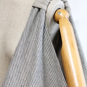 May include: A striped tote bag made of natural linen fabric with a dark blue stripe pattern. The bag is draped over a wooden mannequin arm.