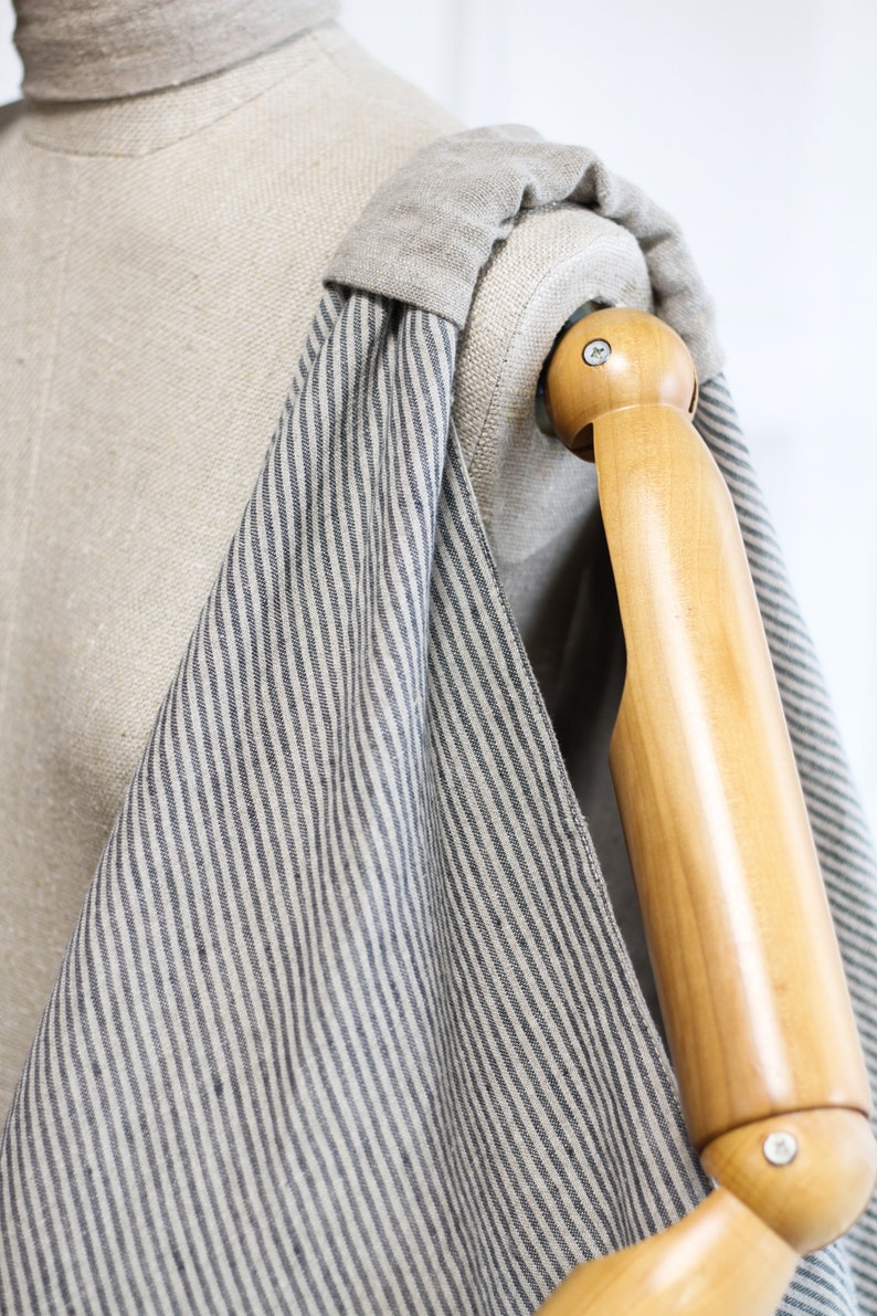 May include: A striped tote bag made of natural linen fabric with a dark blue stripe pattern. The bag is draped over a wooden mannequin arm.