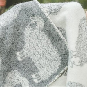 May include: A soft, white and gray throw blanket with a sheep pattern. The blanket is folded in half and draped over a wooden fence.