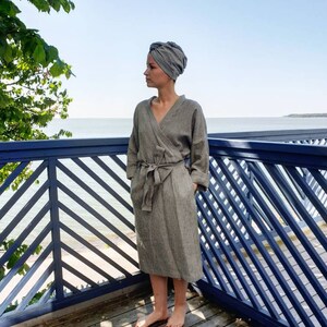 May include: A gray and white striped linen robe with a wrap closure and a matching head wrap. The robe is worn by a person standing on a wooden deck with a blue railing.