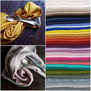 Puede incluir: Un juego de dos servilletas de lino, una amarilla y otra rosa, cada una doblada y colocada sobre una superficie de madera oscura con cubiertos de plata. Las servilletas est&aacute;n hechas de lino natural y tienen un tacto suave y texturizado.