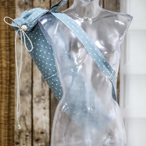 May include: A light blue yoga mat bag with white polka dots and a white drawstring. The bag is hanging on a clear plastic mannequin.