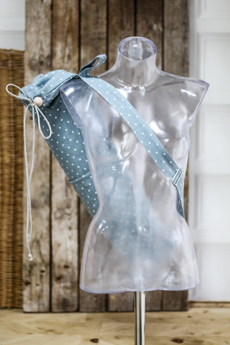 May include: A light blue yoga mat bag with white polka dots and a white drawstring. The bag is hanging on a clear plastic mannequin.