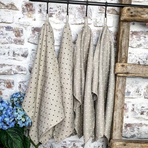 May include: Four beige linen tea towels with black polka dots hanging on a black metal rod. The towels are folded and hanging in a row.