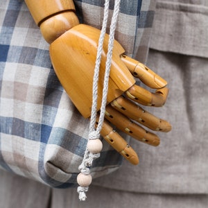 May include: A wooden hand model holding a blue and brown plaid tote bag with a rope handle and wooden beads.