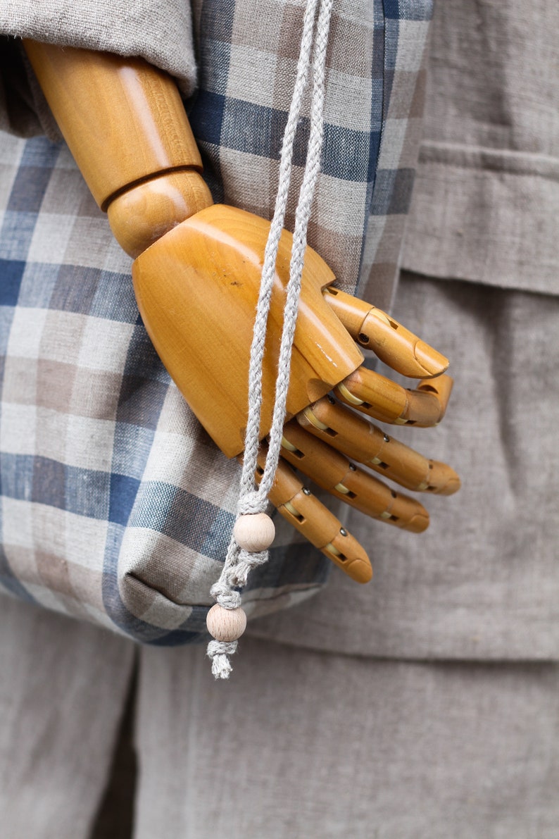 May include: A wooden hand model holding a blue and brown plaid tote bag with a rope handle and wooden beads.
