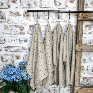 May include: Four beige kitchen towels with black polka dots hang on a black metal rack against a white brick wall. The towels are folded and hanging in a row.