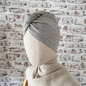 May include: A gray and white striped turban made of fabric. The turban is tied in a knot on top of the head.