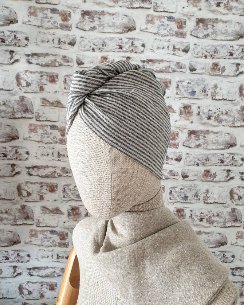 May include: A gray and white striped turban made of fabric. The turban is tied in a knot on top of the head.